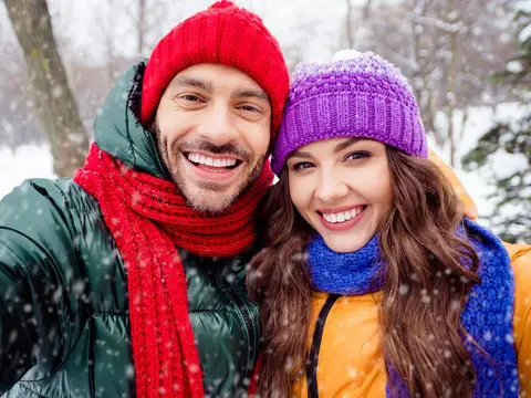 A couple in winter hats and scarves smiling together in falling snow