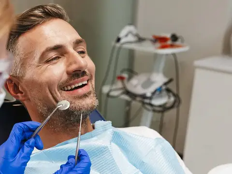 A man smiling in the dental chair as the dentist checks a restored tooth