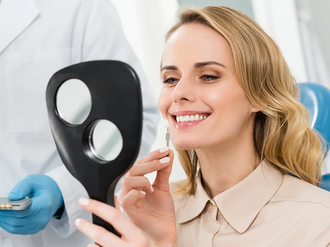 A woman looking at her new smile in a hand mirror held by the dentist