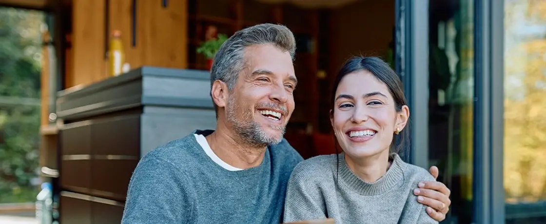 A smiling couple holding coffee mugs on a sunny back porch