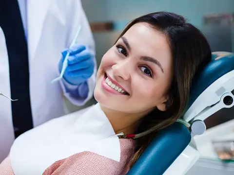 A relaxed patient smiling in the dental chair while the dentist prepares an instrument
