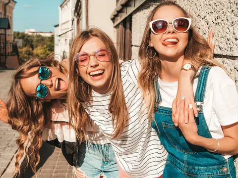 Three young women laughing together on a sunny street