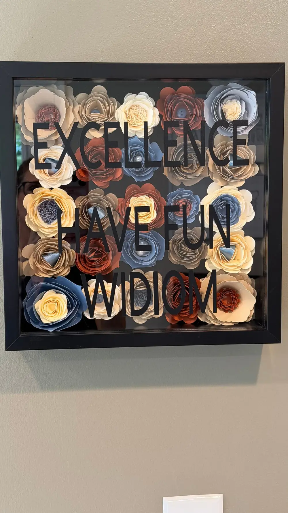 Paper flowers frame the words Excellence, Have Fun, and WIDIOM on the office wall