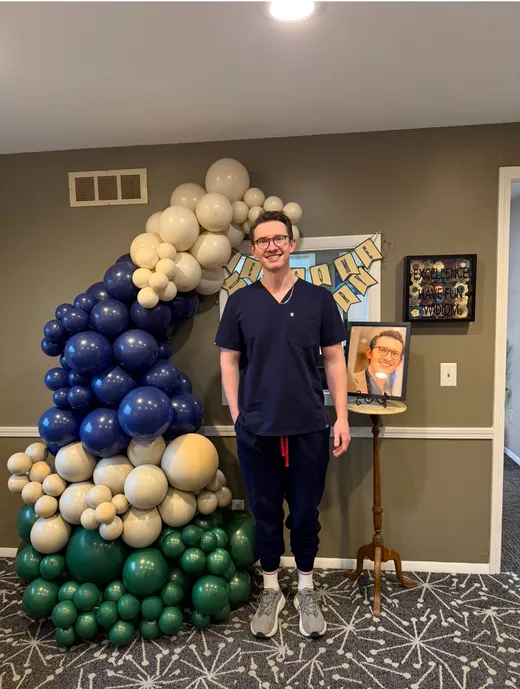 Dr. Berry beside a balloon arch and a framed portrait at his welcome party at the practice