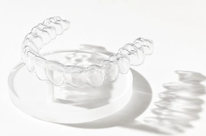 A clear aligner standing in its open travel case, backlit on cream stone
