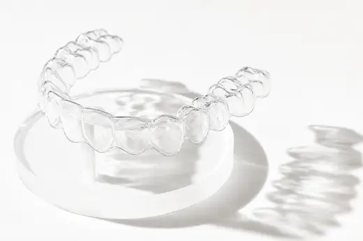 A clear aligner standing in its open travel case, backlit on cream stone